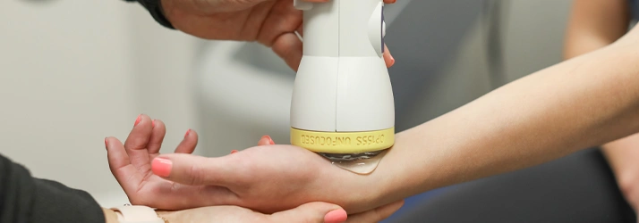 Handheld SoftWave therapy device applied to a person’s forearm